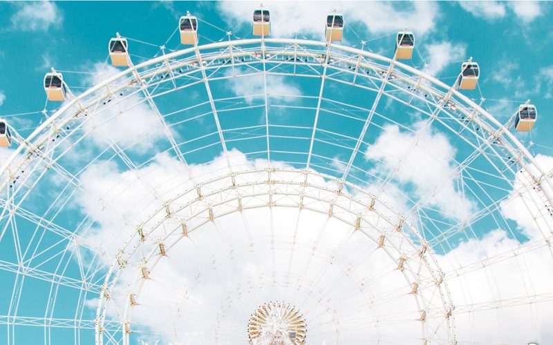 Looking up at a white observation wheel against a bright blue sky
