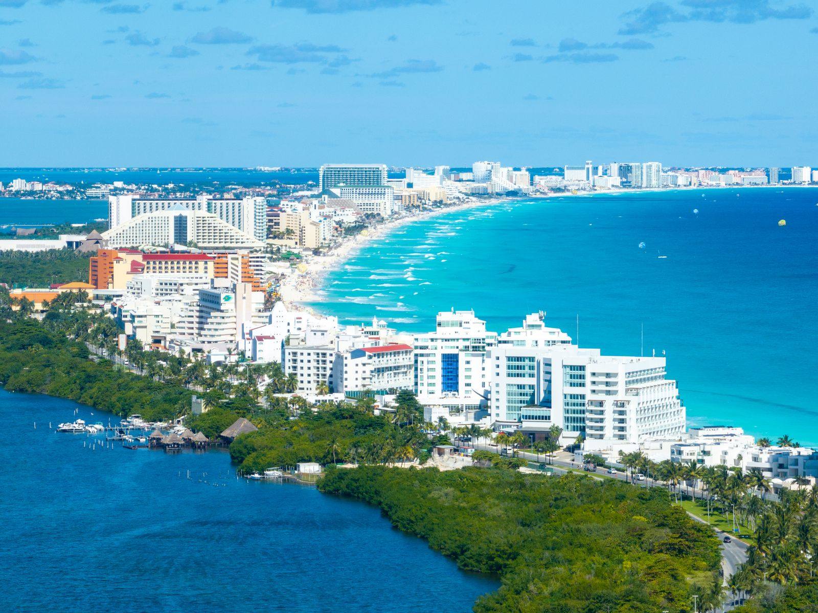 Aerial view of the Cancun Hotel Zone: white resort towers along a turquoise Caribbean beach, with the lagoon and mangroves in the foreground