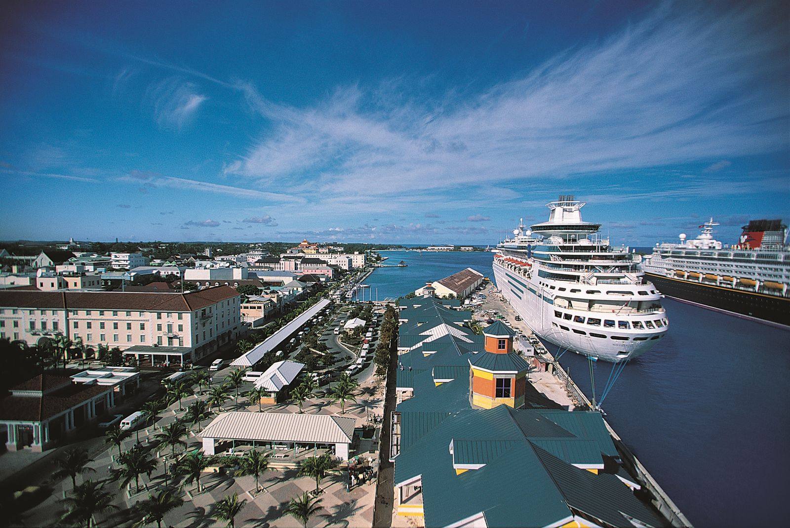 Cruise ship docked at a pier beside a waterfront town with green roofs and palm-lined streets