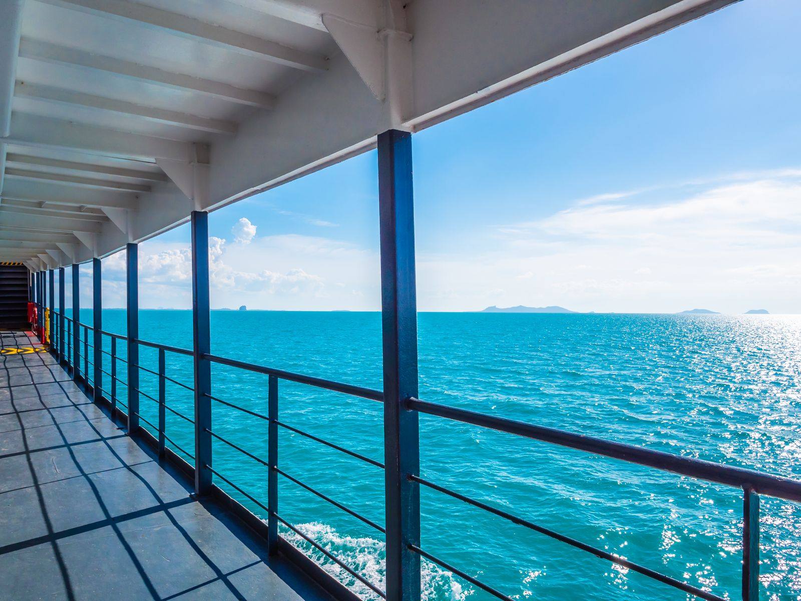 Covered outdoor deck with railings on a ship, looking out over bright turquoise sea