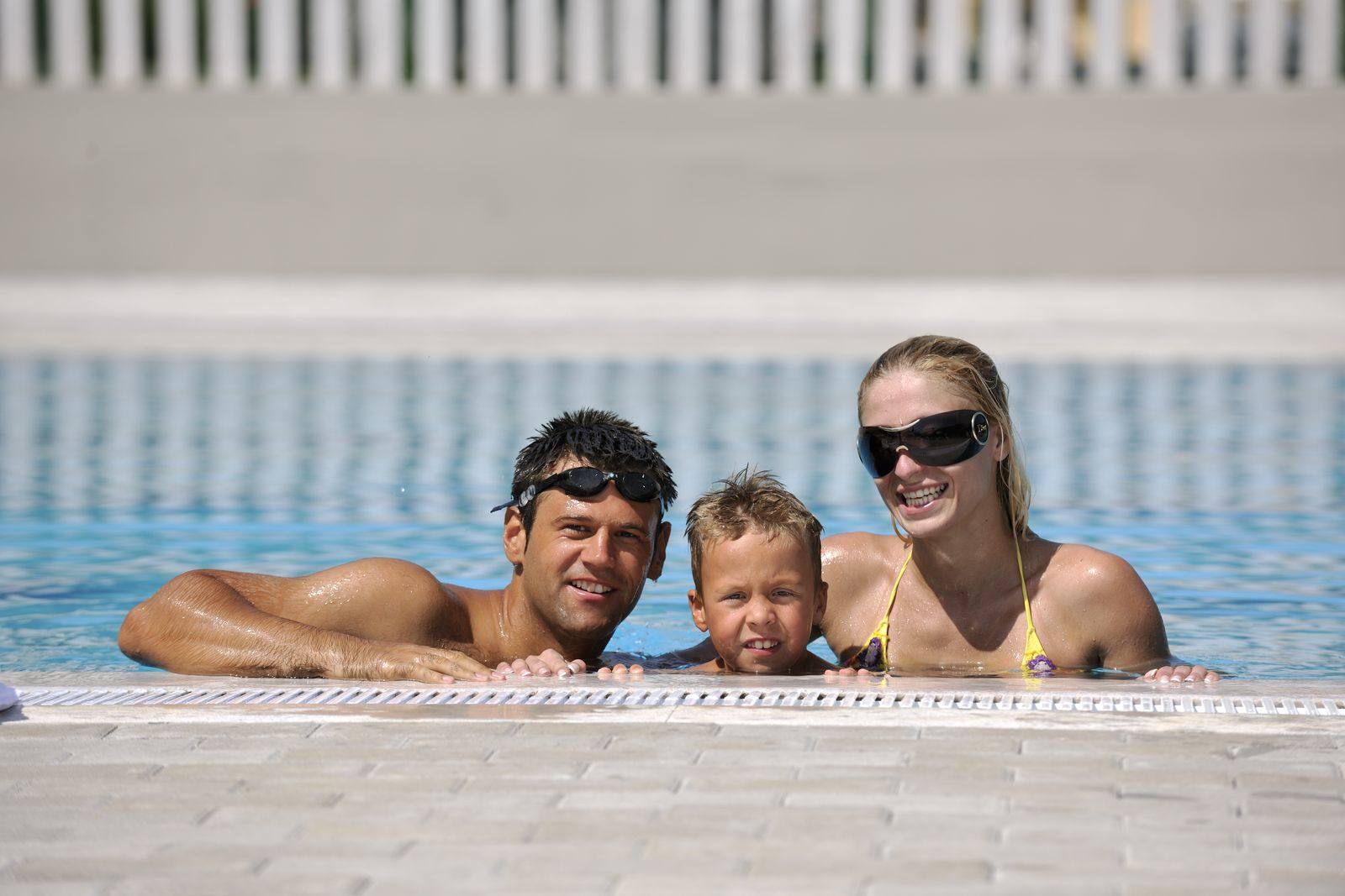 Mom, dad and a young boy smiling at the edge of a swimming pool