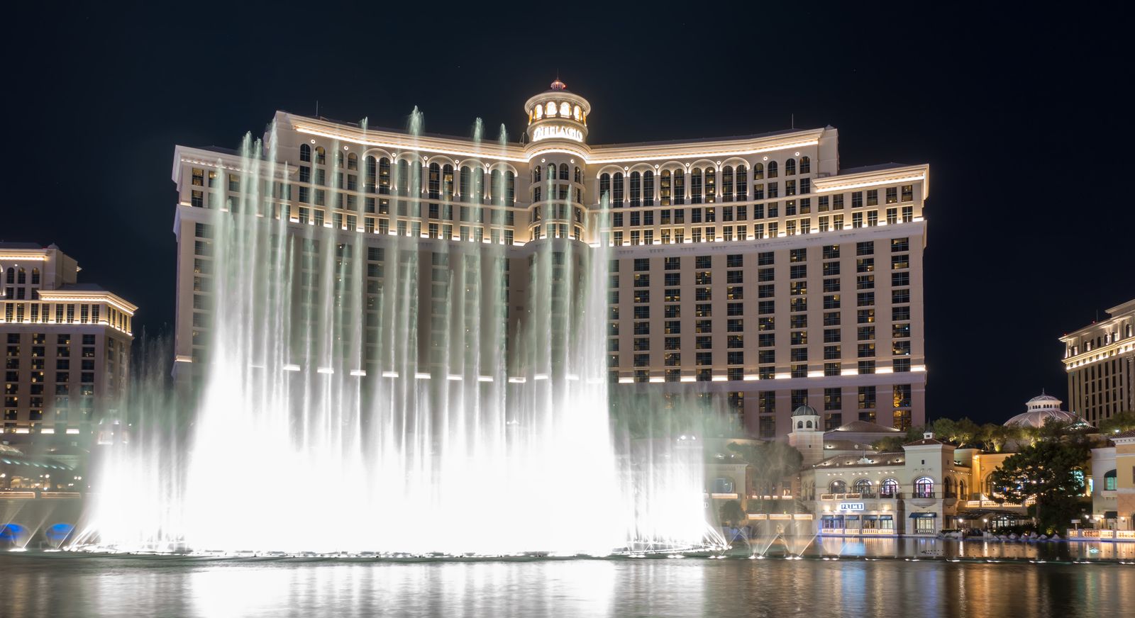The Bellagio fountain show in Las Vegas at night, with tall white water jets in front of the lit hotel facade