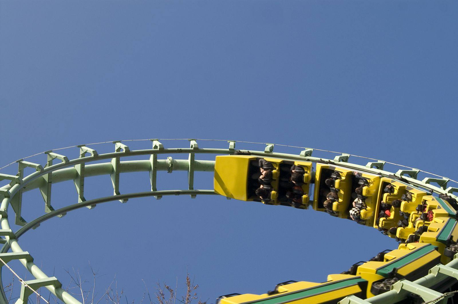Yellow roller coaster train full of riders rounding a looping green track against a blue sky