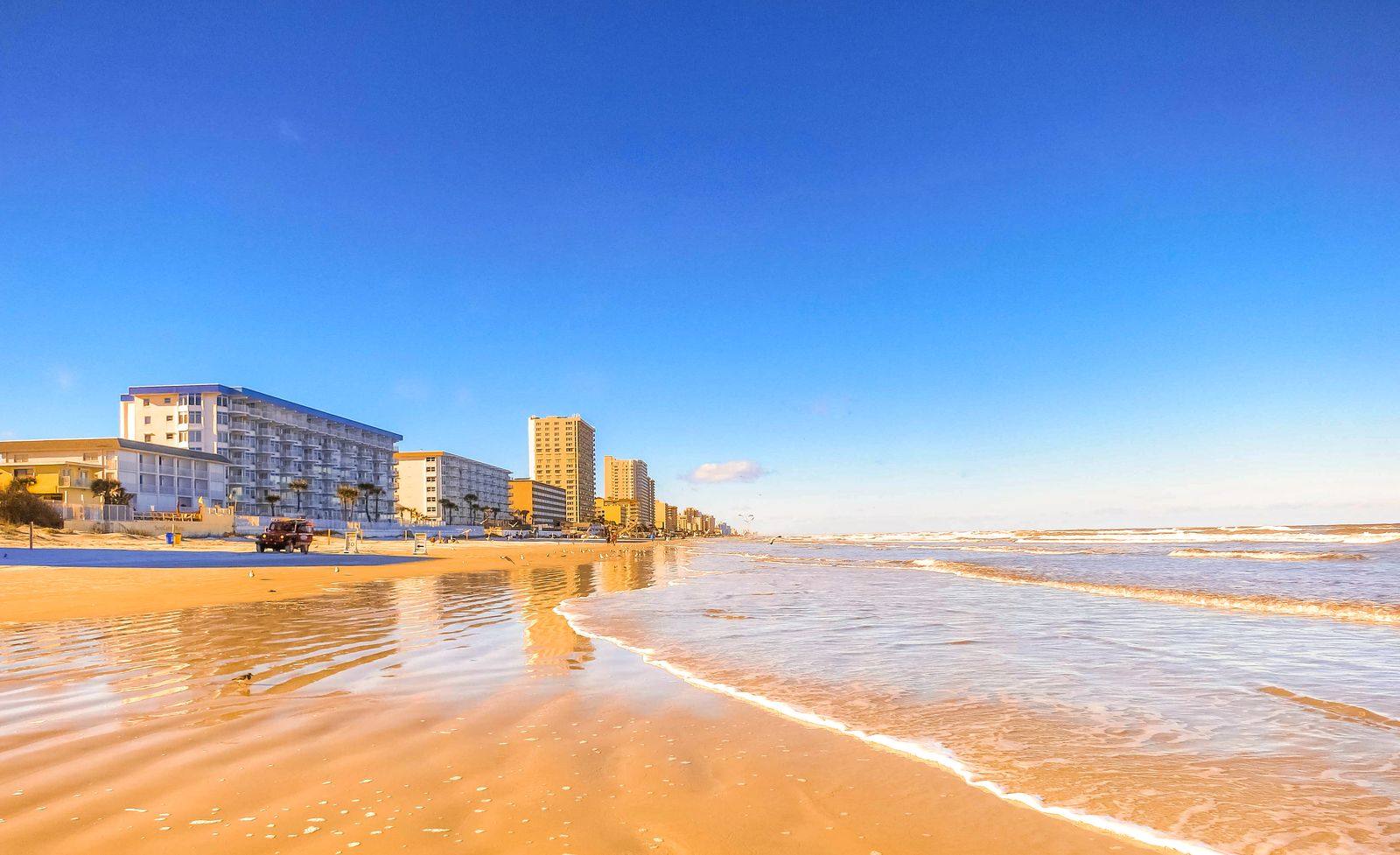 Wide sandy beach at Daytona Beach, Florida, with gentle surf and a row of beachfront hotels under a clear blue sky