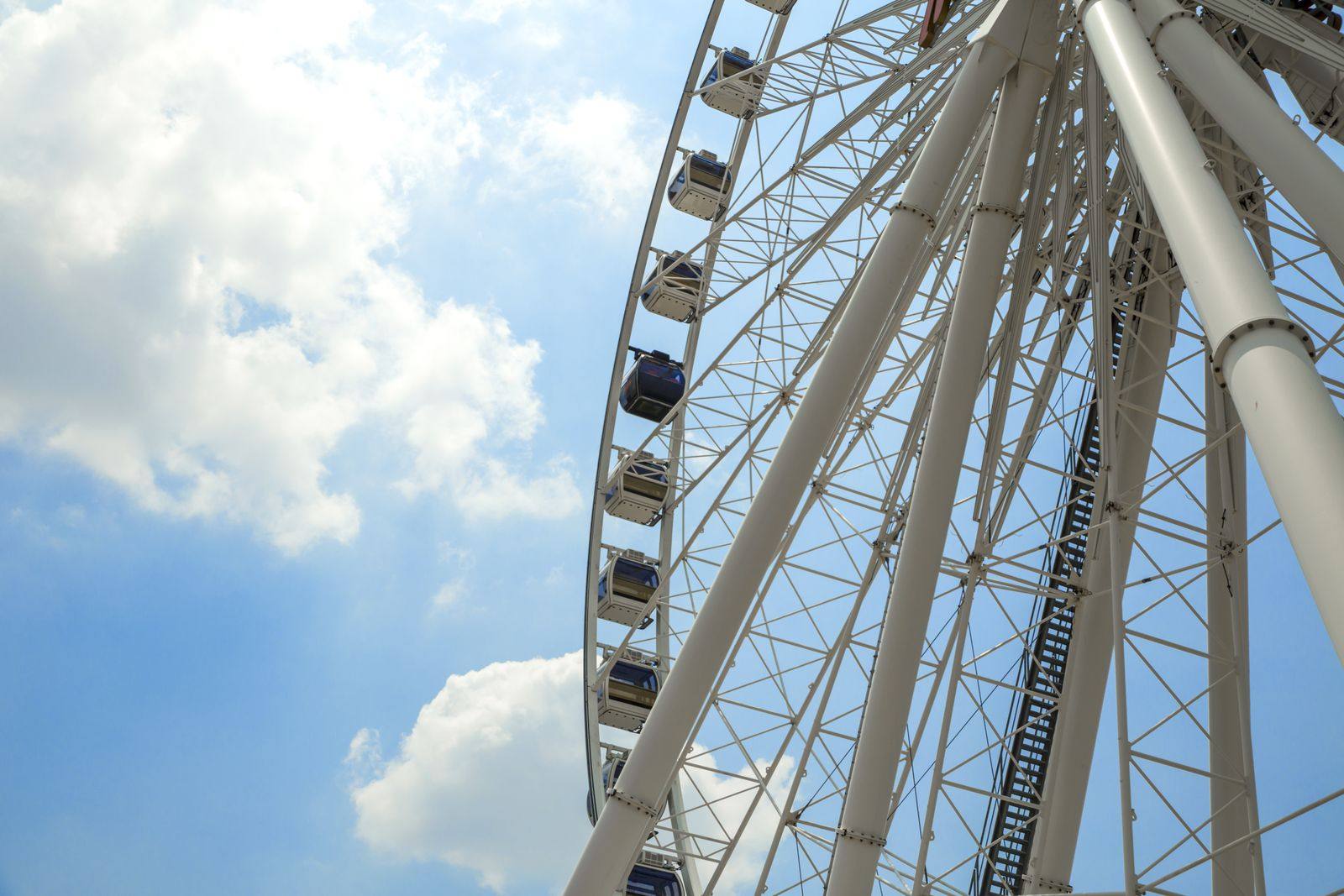 Large white observation wheel with enclosed gondolas, seen from below against a blue sky with white clouds