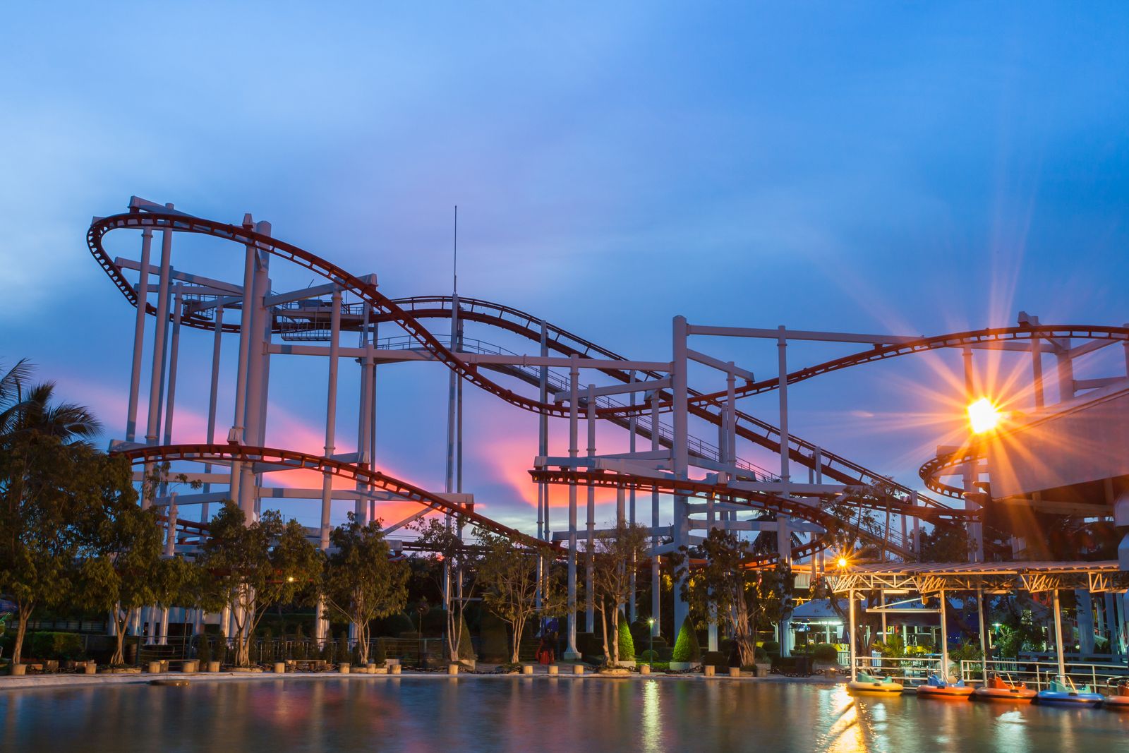 Roller coaster tracks at dusk beside a lake, under a blue and pink sky