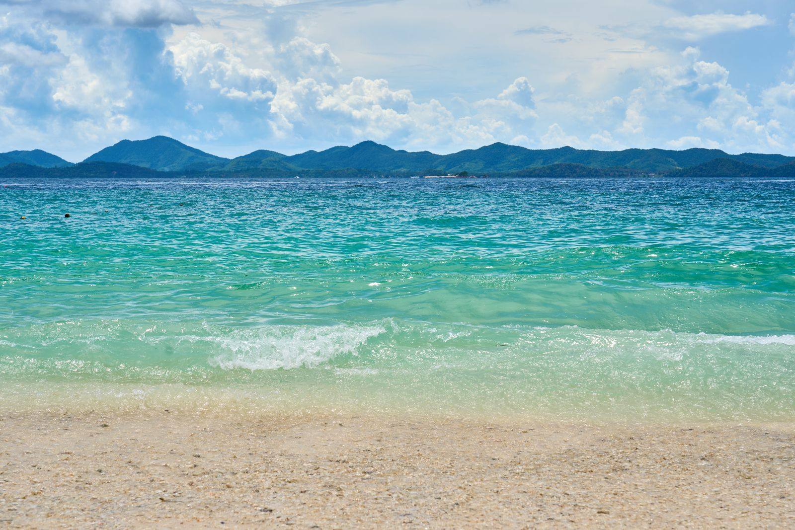 Turquoise waves rolling onto a sandy beach, with green mountains along the far shore
