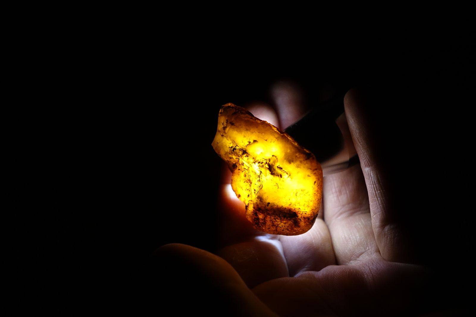 A piece of golden amber glowing in an open hand against a dark background
