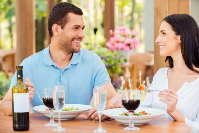 Smiling couple having lunch at an outdoor table, with salads and glasses of wine