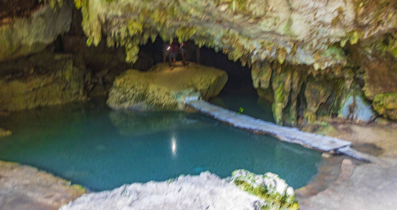 Still turquoise pool inside a limestone cave cenote in Mexico, with a narrow walkway at the water's edge