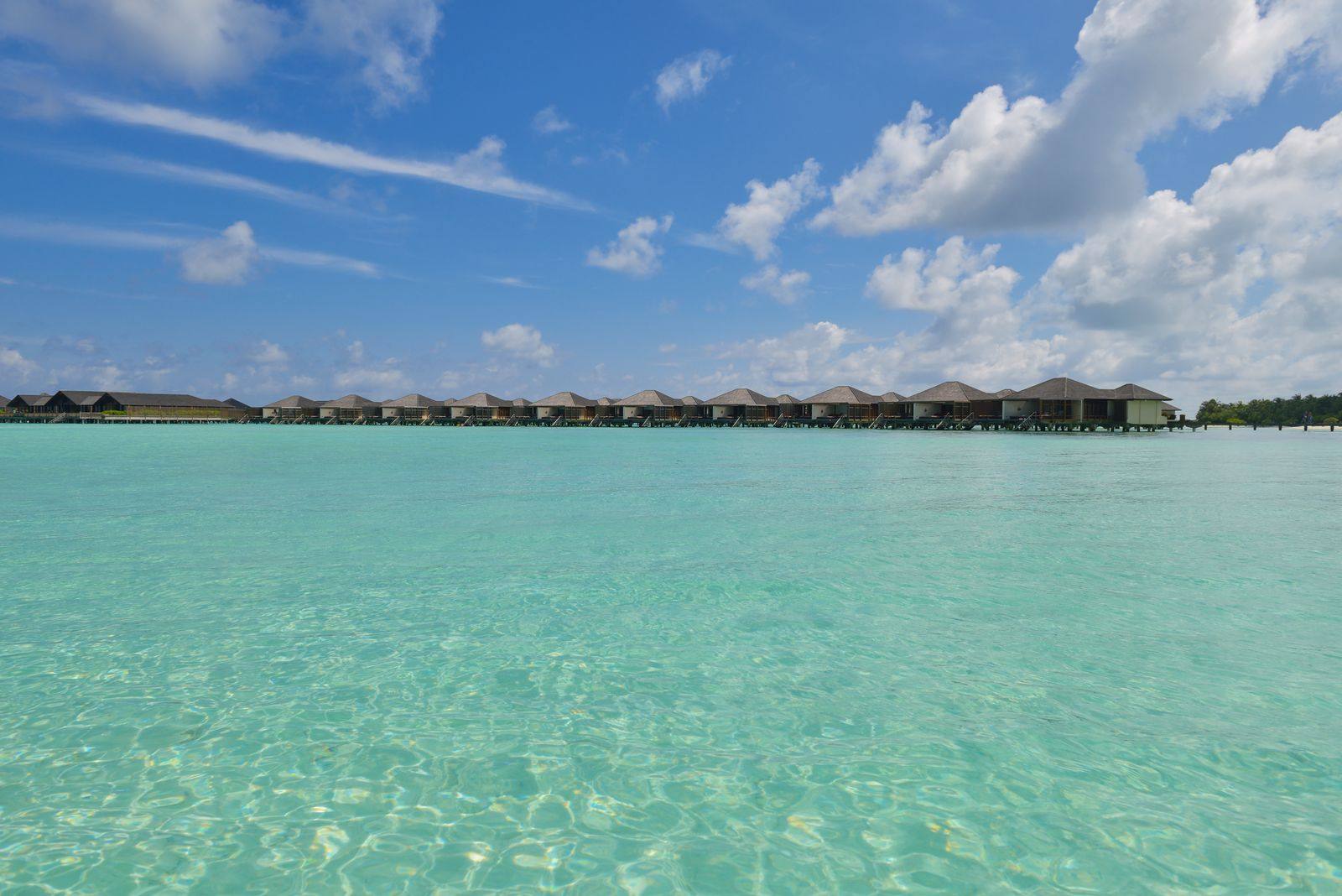 Overwater villas across a shallow turquoise lagoon under a blue sky with white clouds
