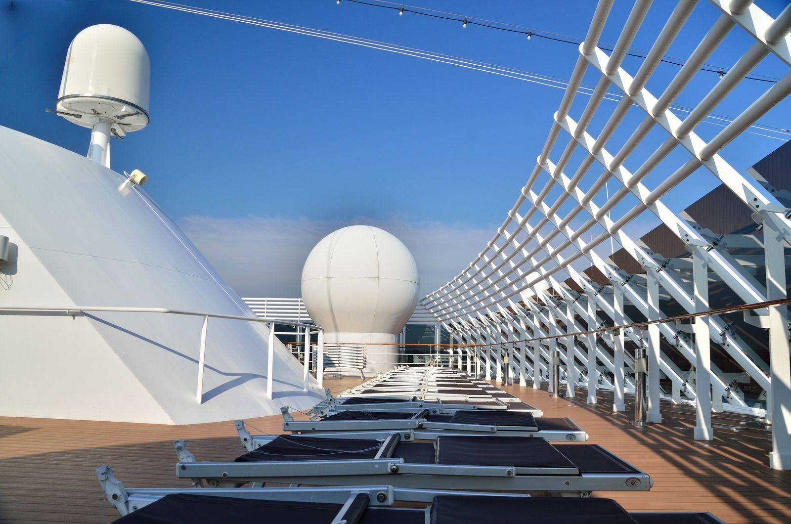 Sun loungers lined up on the top deck of a cruise ship under a clear blue sky