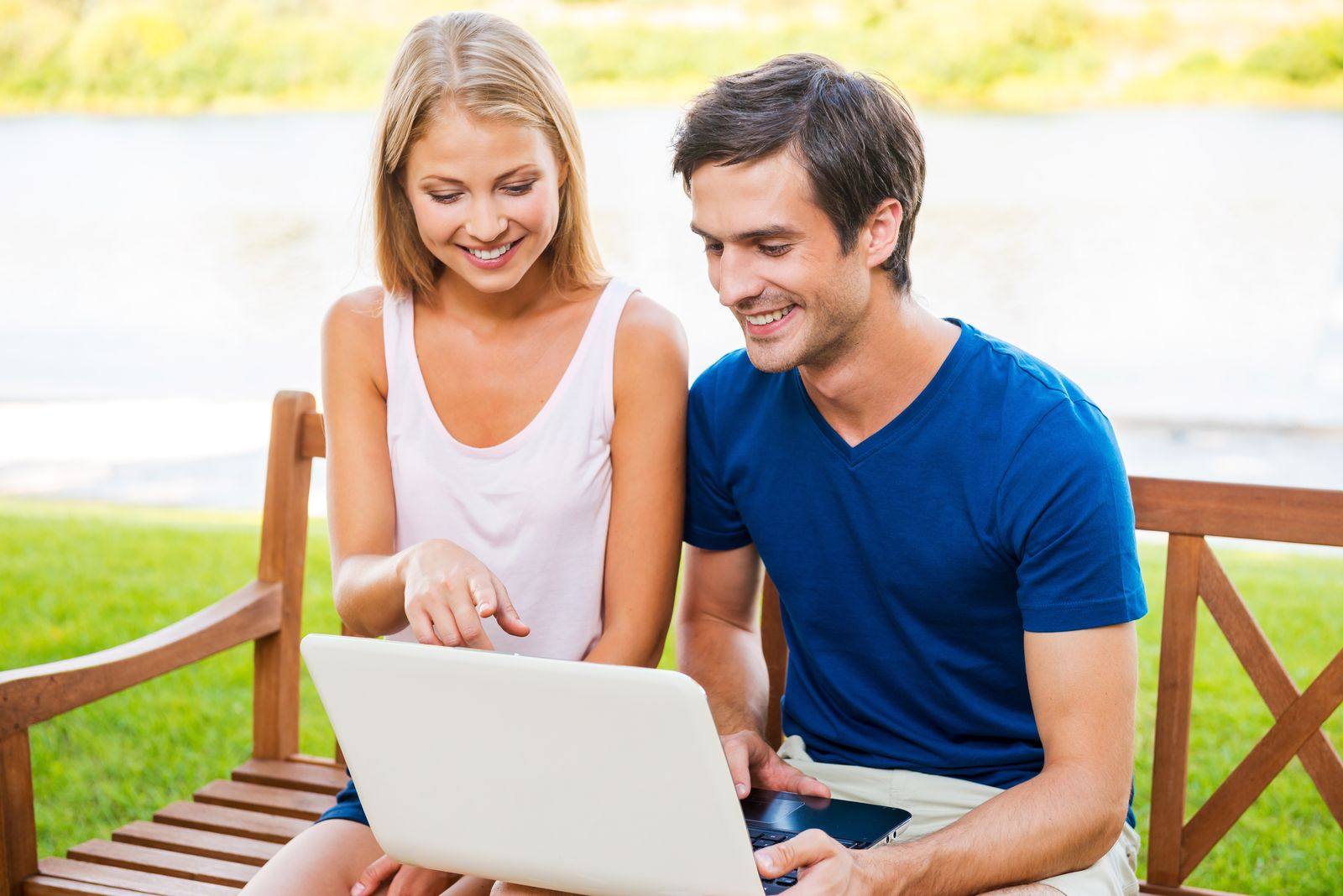 Smiling couple on a wooden bench looking at a laptop together